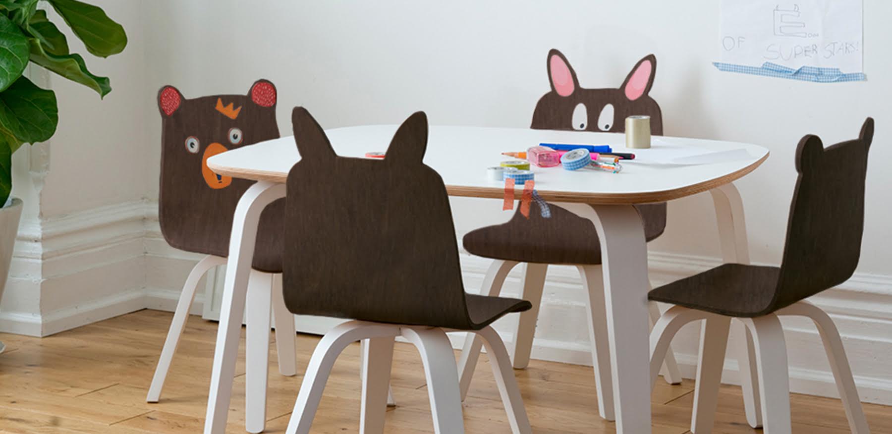 Children’s table and chairs with animal faces and ears, art supplies on the table, in a bright room.