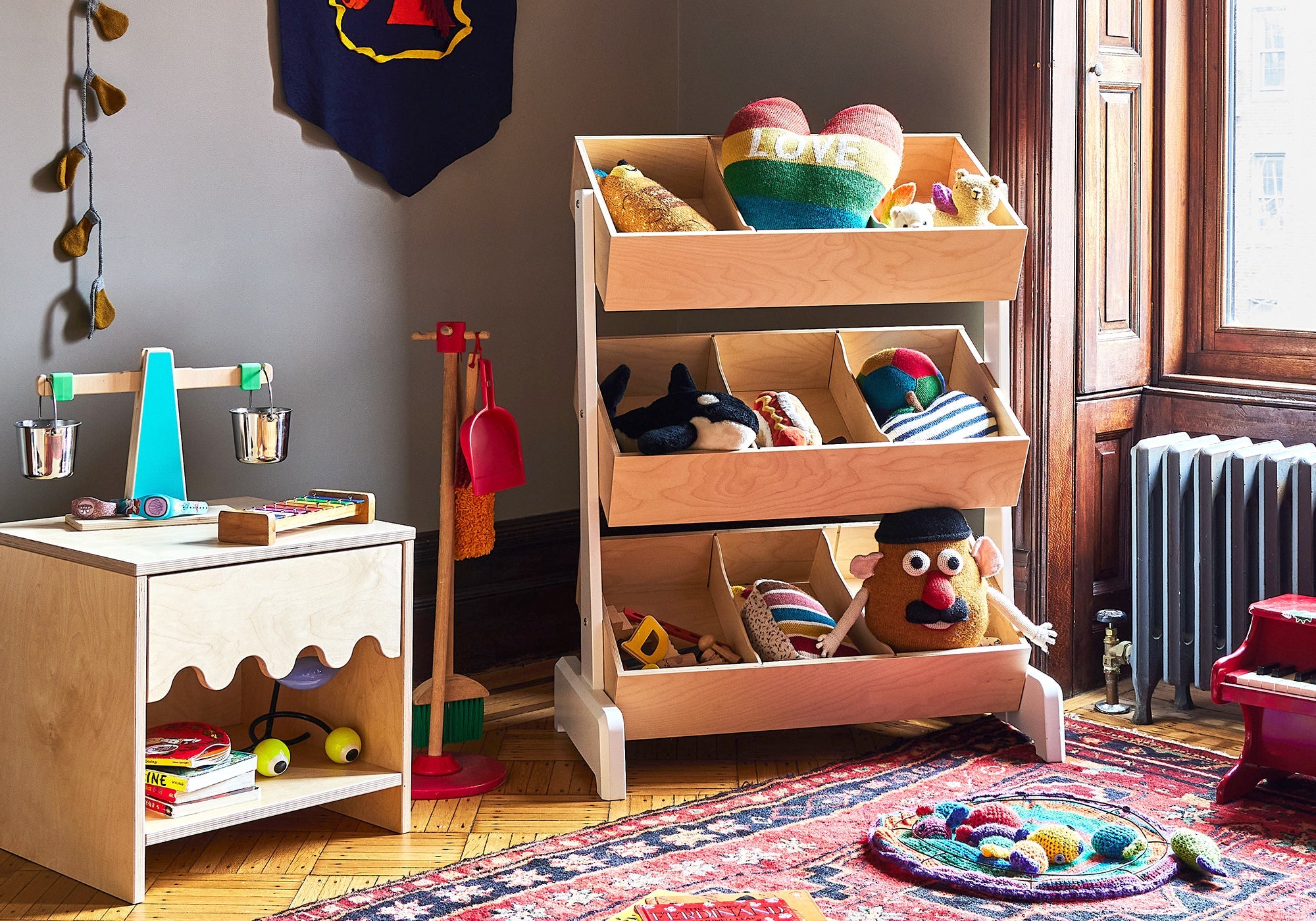 A cozy playroom with toy shelves, a balance scale, stuffed toys, and a colorful rug by a sunny window.