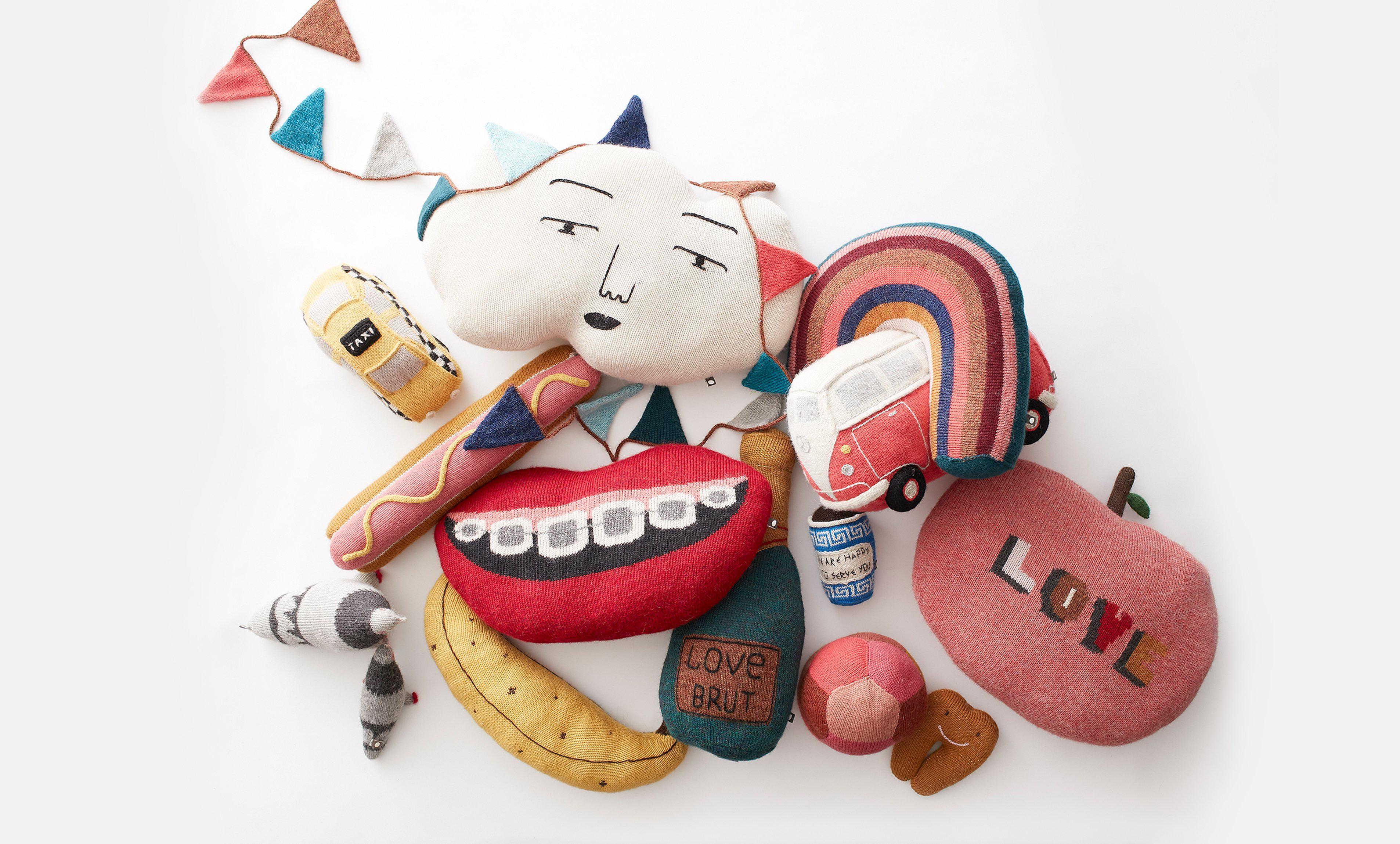 Colorful plush pillows shaped like a cloud face, rainbow van, lips, hotdog, apple, banana, and small bunting.