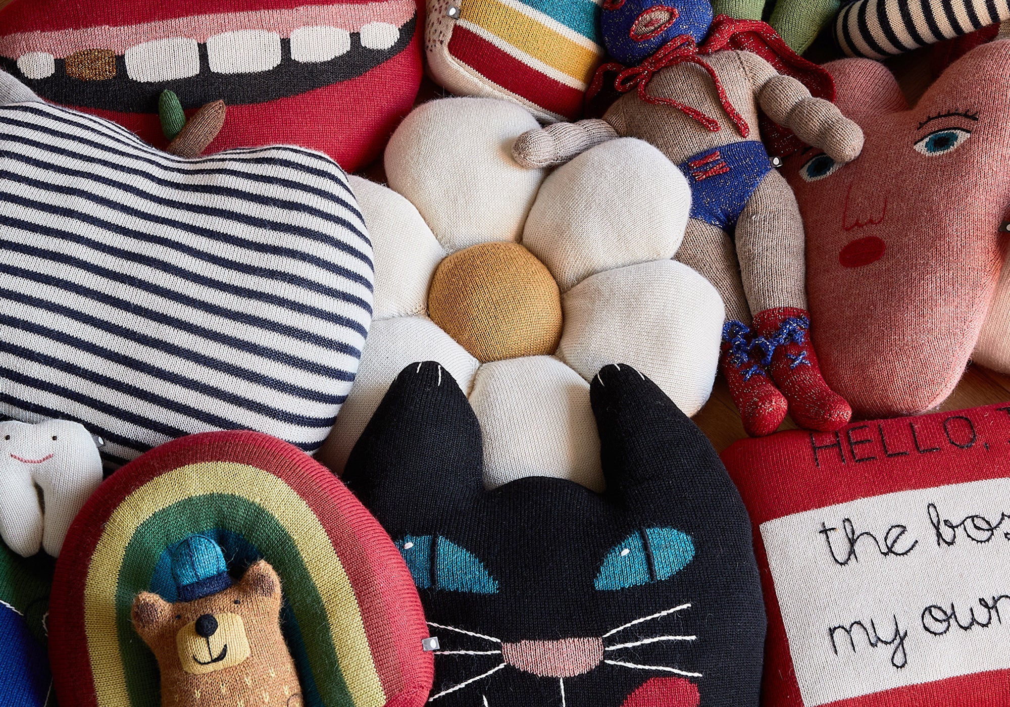 Assorted colorful plush toys, including a cat, rainbow, tooth, flower, and faces, arranged together closely.
