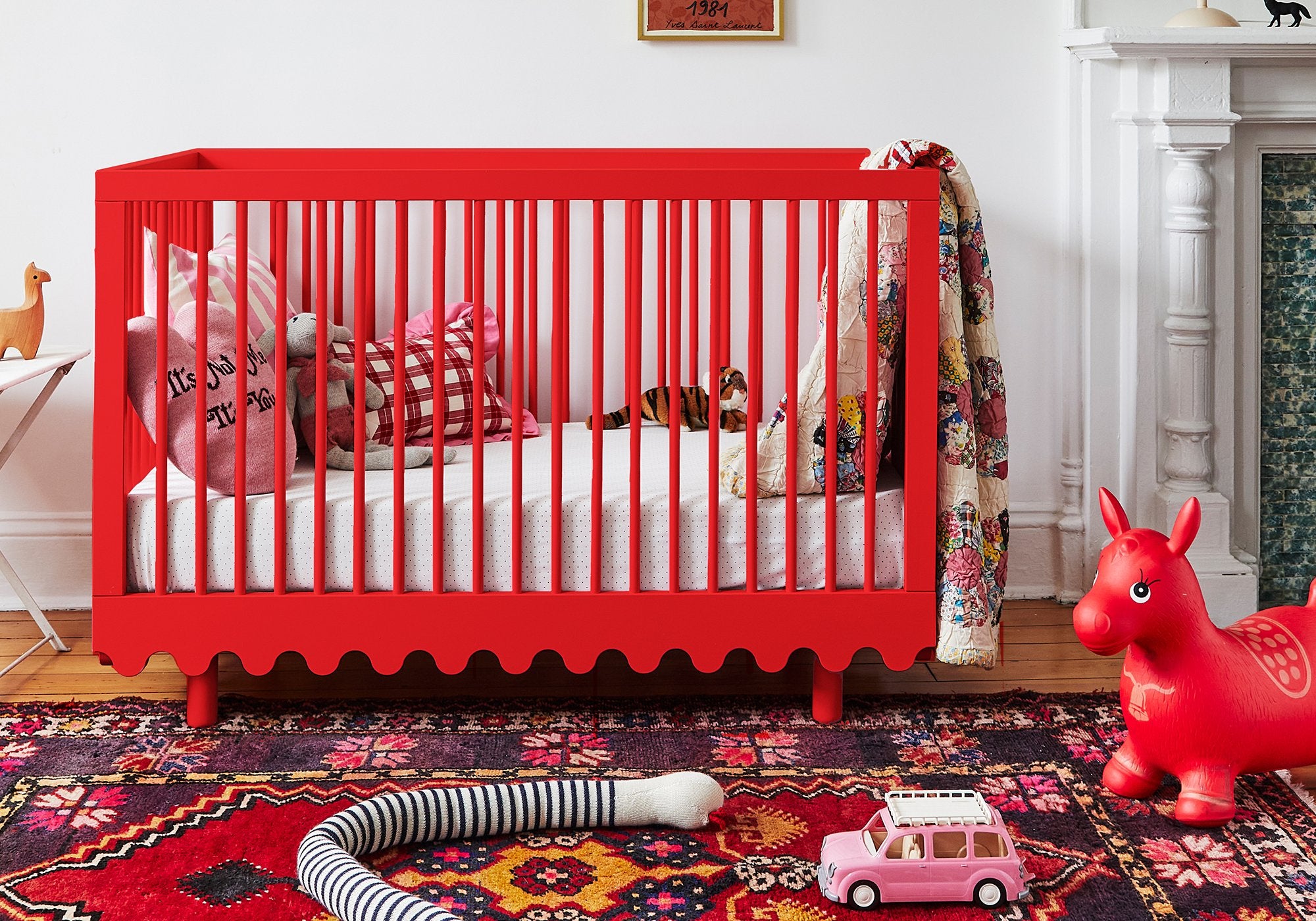 A bright red crib with pillows and toys in a colorful, cozy nursery with a patterned rug and playful decor.