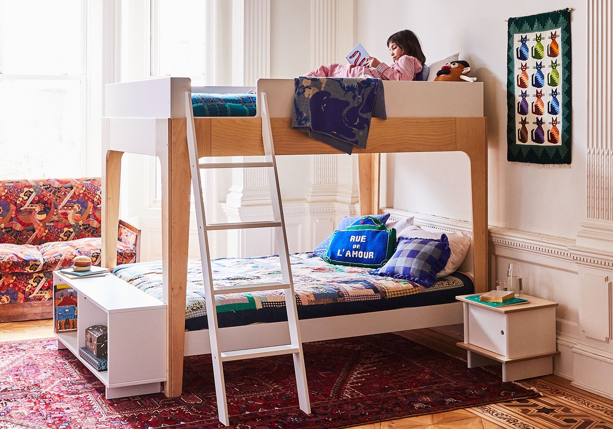 A child reads on the top bunk of a modern bunk bed in a colorful, cozy bedroom with toys and bright decor.