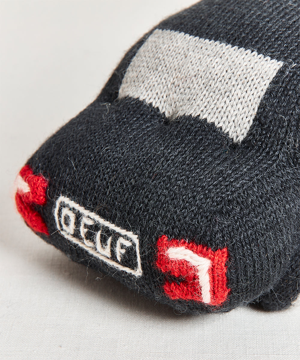 My Ride Pillow: A knitted toy car featuring a black body, gray windows, red taillights, and white "DEUF" text on the back, displayed on a light surface.