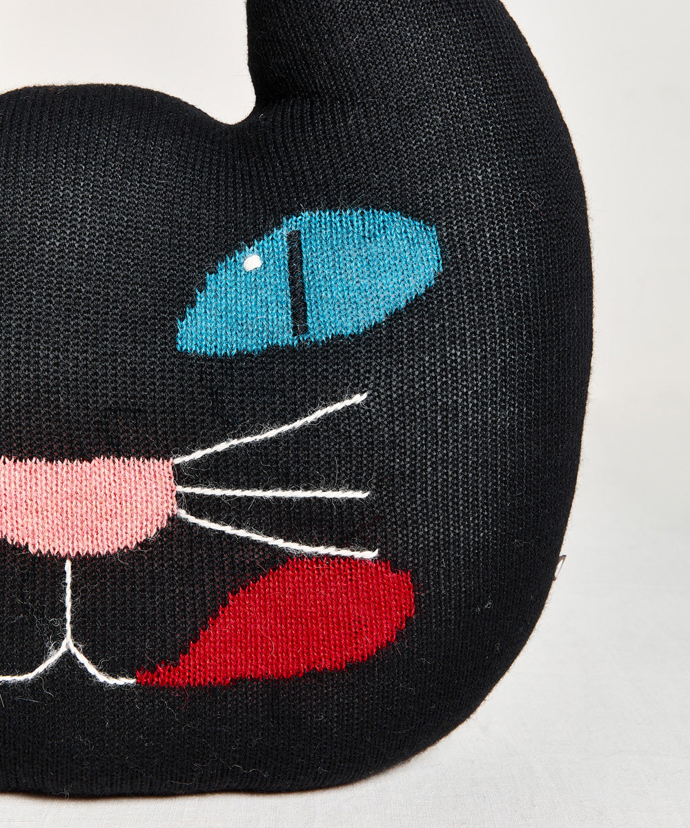 Close-up of the Black Cat Pillow: a black knit plush toy with blue eyes, pink nose, white whiskers, and a red mouth.