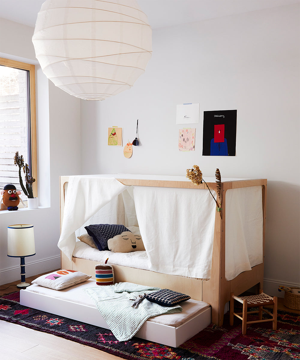 A cozy kids bedroom featuring the Perch Nest Bed with colorful pillows, a white canopy, decorated walls, and a patterned rug.