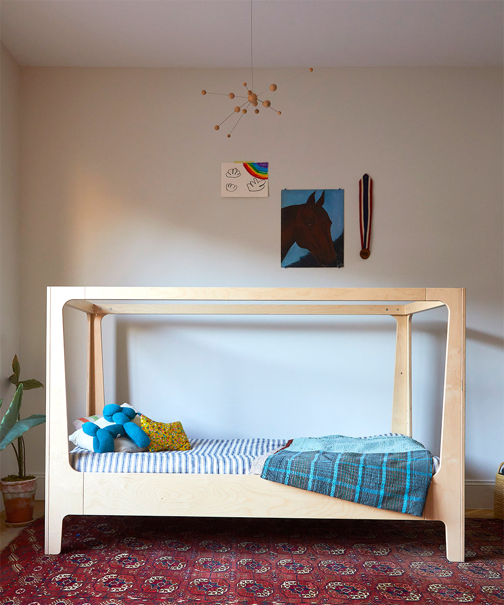 Minimalist bedroom featuring the Perch Nest Bed, blue and striped bedding, a plant, wall art, and a red patterned rug.