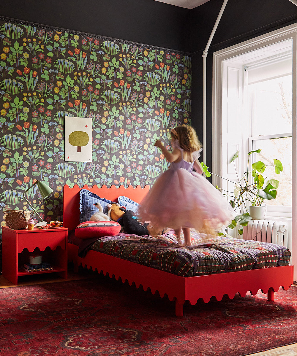 A child twirling on a Moss Twin Bed in a colorful bedroom with floral wallpaper and a sunlit window.