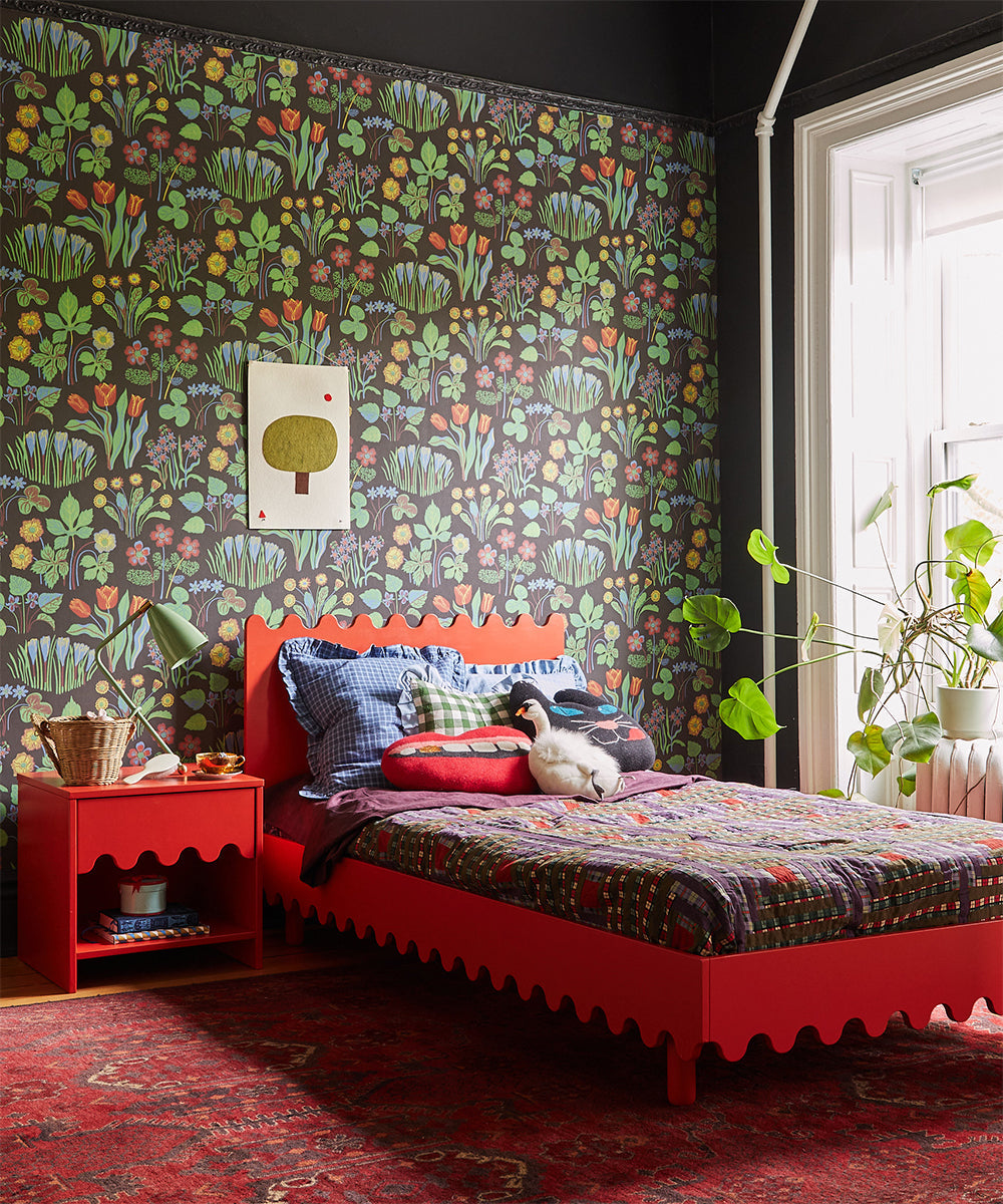 Eclectic bedroom with vibrant floral wallpaper, red bed, Moss Nightstand, and plants by a window.