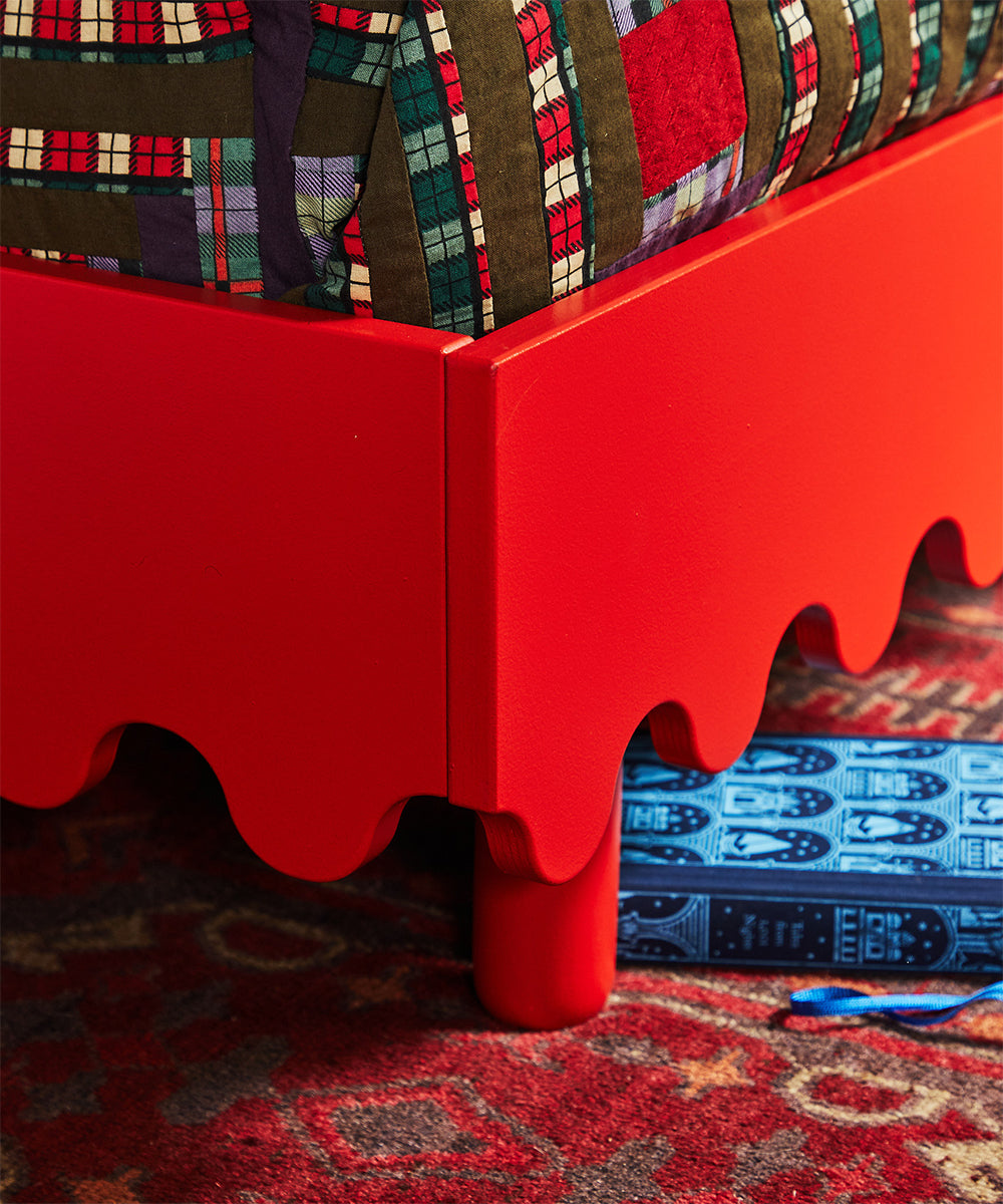Moss Twin Bed with scalloped edges, plaid quilt, and blue patterned book on a red patterned rug.