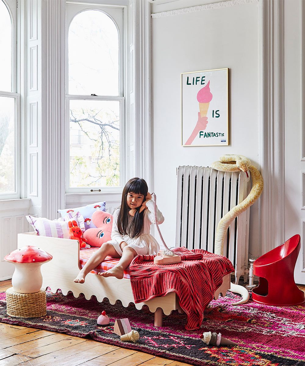 A child sits on a Moss Toddler Bed in a colorful room with large windows, toys, and a Life is Fantastic poster.