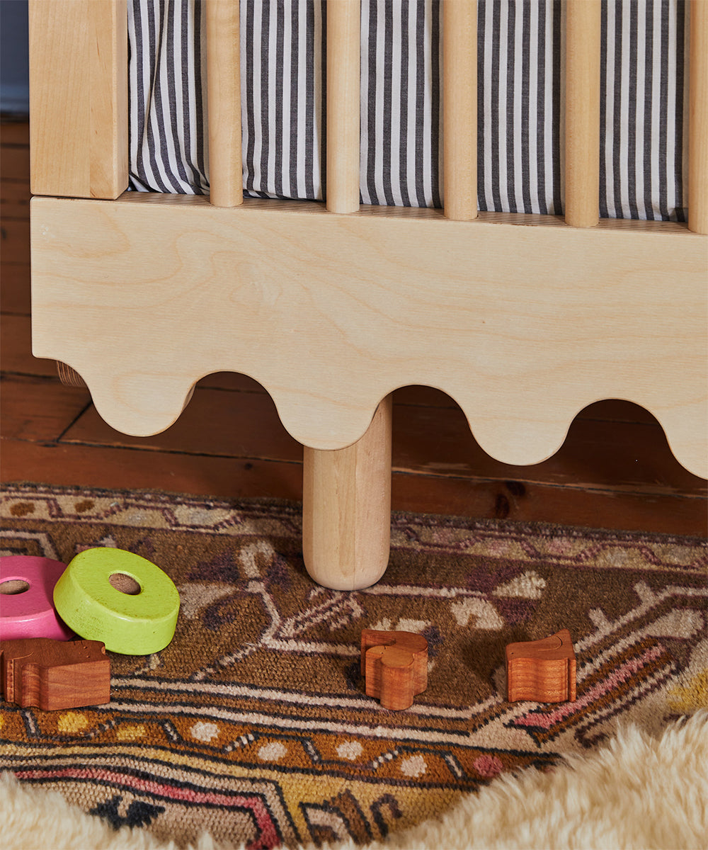 Moss Crib with a striped mattress surrounded by colorful toys on a patterned rug.