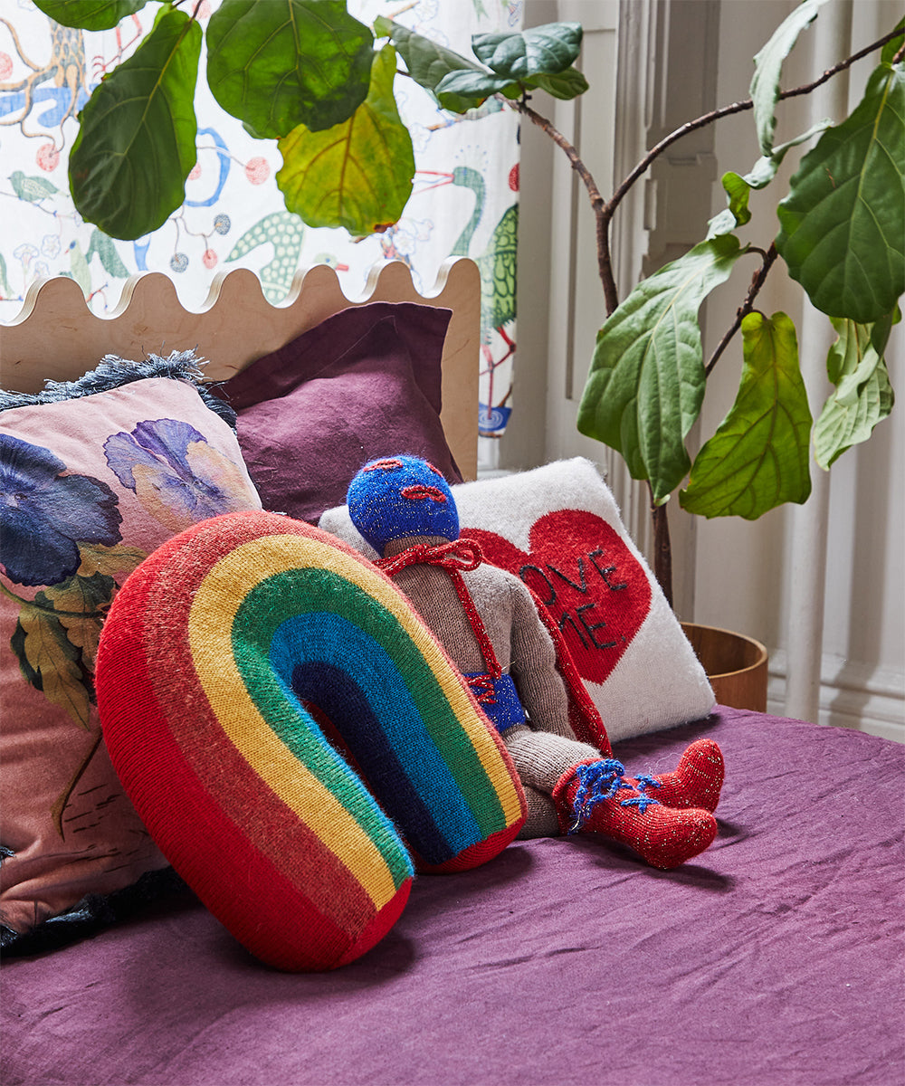 The Moss Twin Bed features a rainbow pillow, colorful doll, and heart-themed decor, complemented by a large potted plant near the window.