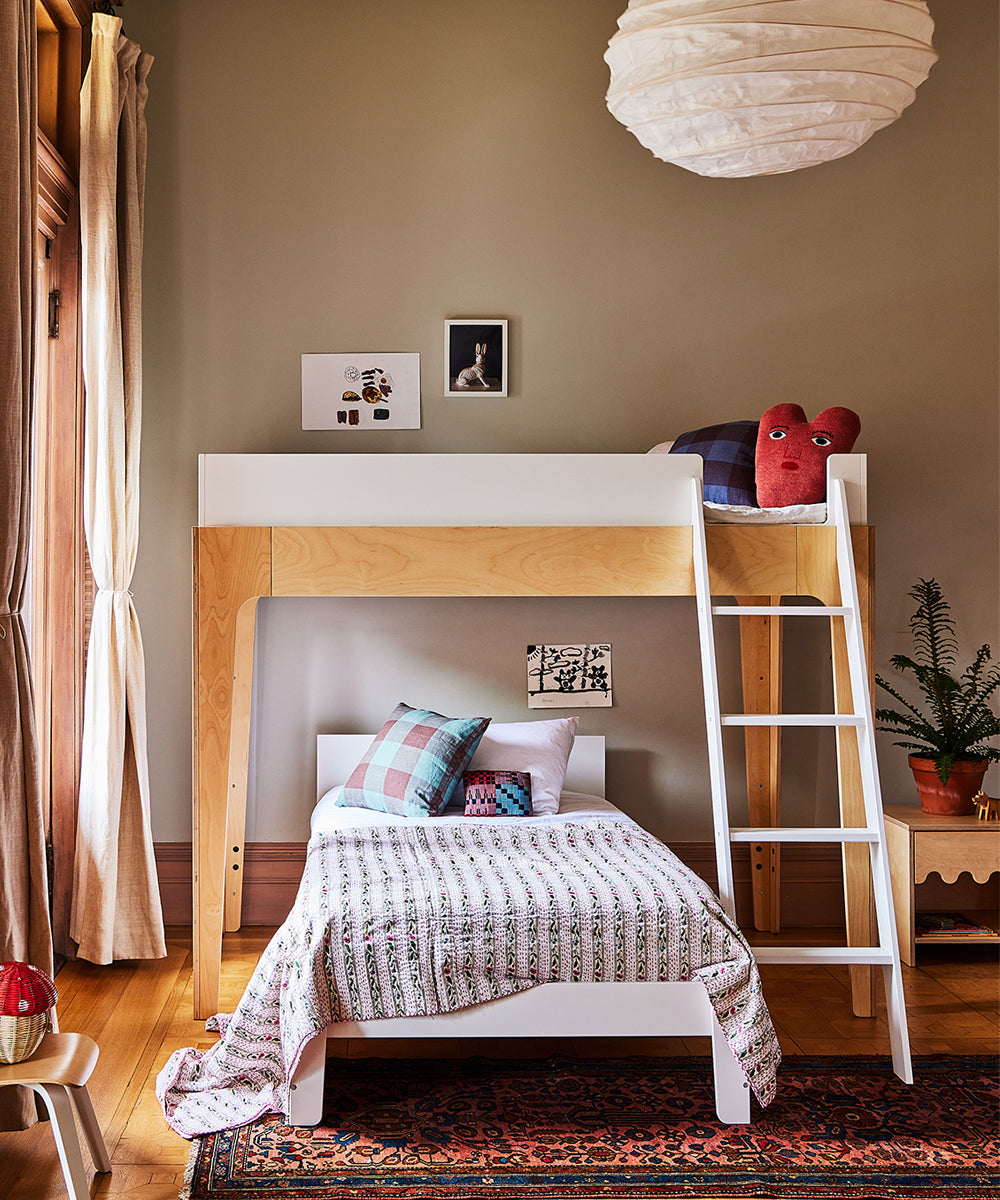 A childrens room featuring the Perch Twin Bed with ladder, patterned bedding, a heart-shaped pillow, wall art, and a small plant.