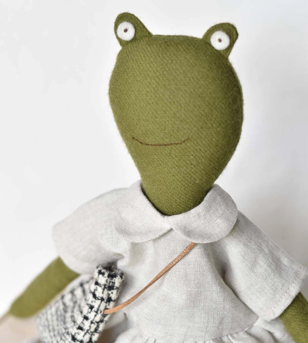 Fern le Frog is a stuffed frog doll in a light dress holding a small black-and-white patterned bag.