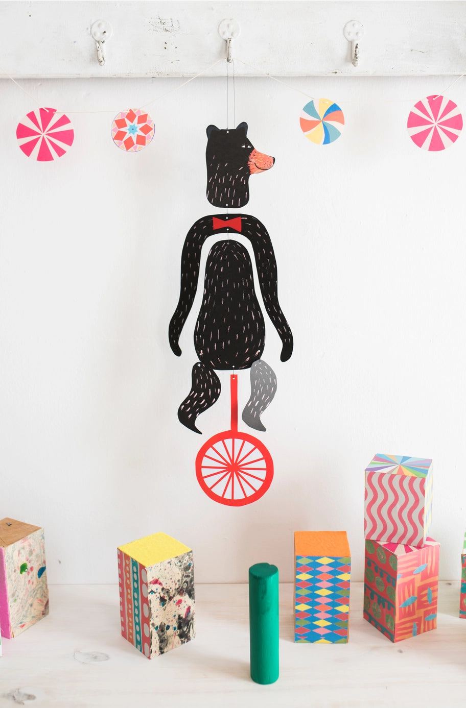 The Le Mobile - Circus Bear features a paper cutout of a bear on a unicycle hanging above colorful blocks and decorations on a white background.