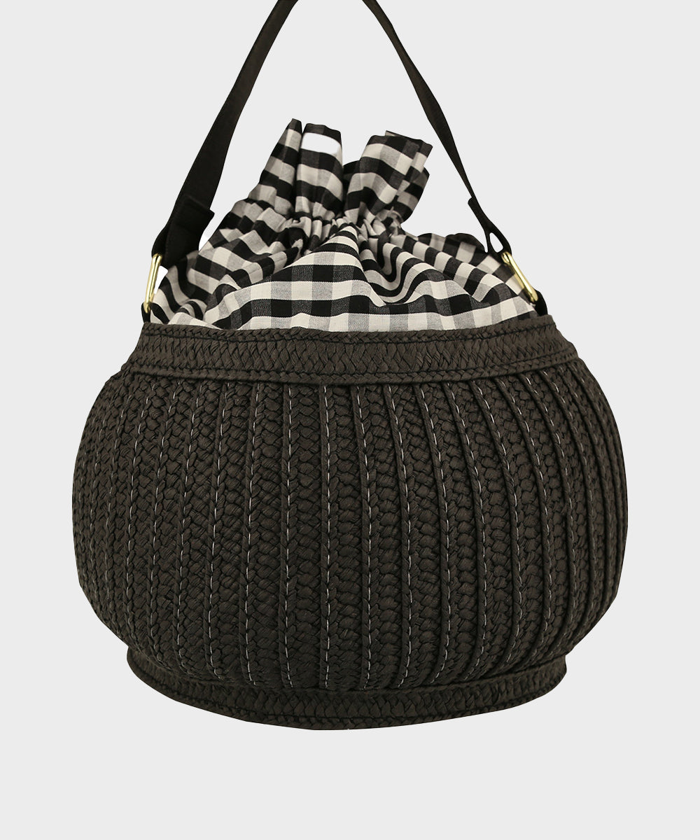 The Le Cat Basket Bag is a round black woven bag with a black and white checkered drawstring closure and black handle.