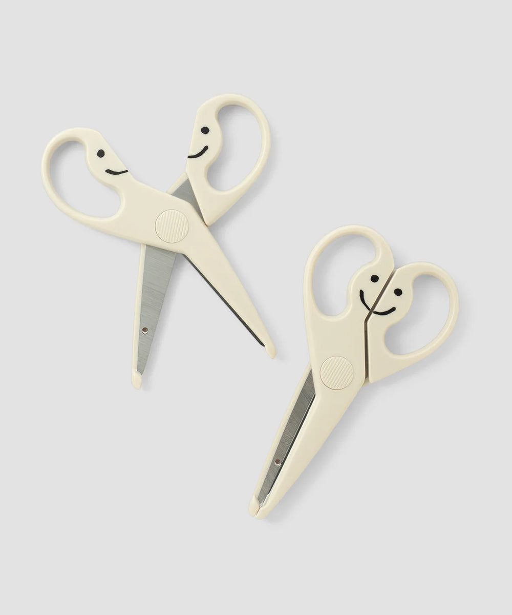 Two Le Gentle Scissors with smiling faces on white handles, placed on a light gray background.