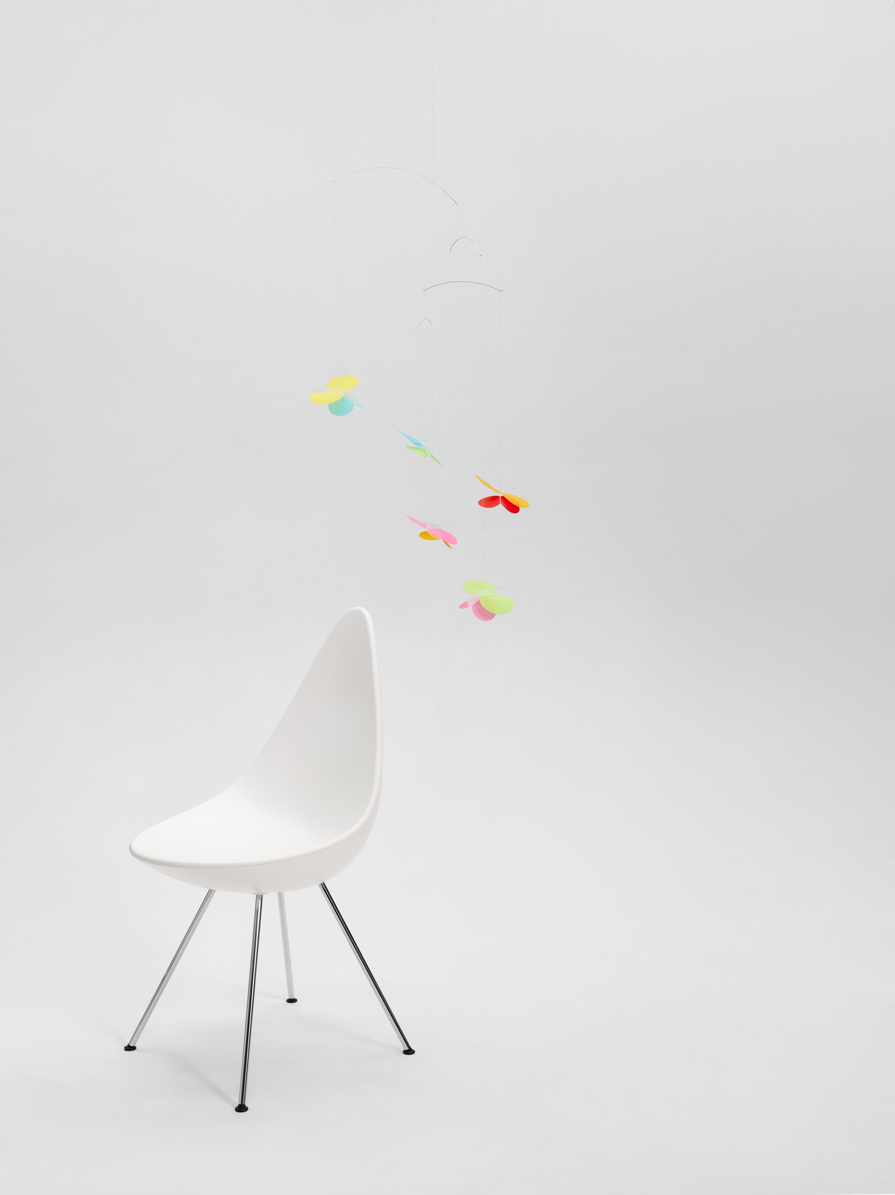 A white modern chair sits beneath the Butterflies mobile in a minimal, bright setting.