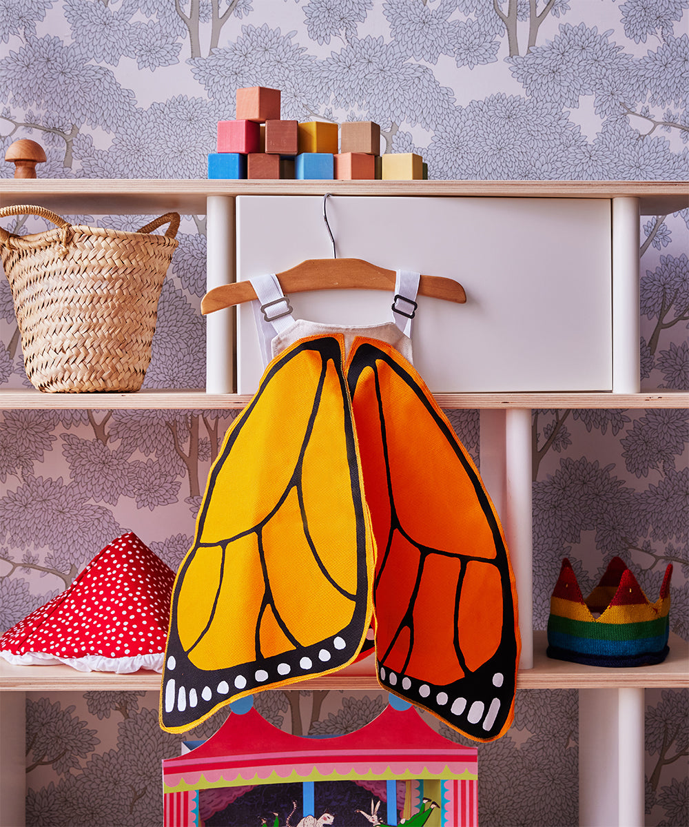 Children’s playroom shelf with Le Monarch Butterfly Wings, wooden blocks, a basket, crown, and red spotted hat.