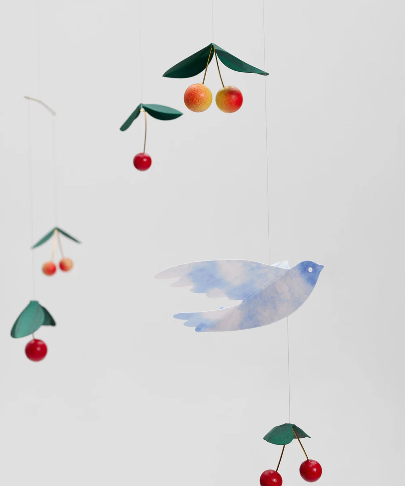 Le Mobile - Cherry Bird: a hanging mobile featuring a blue bird, red cherries, and green leaves set against a plain backdrop.