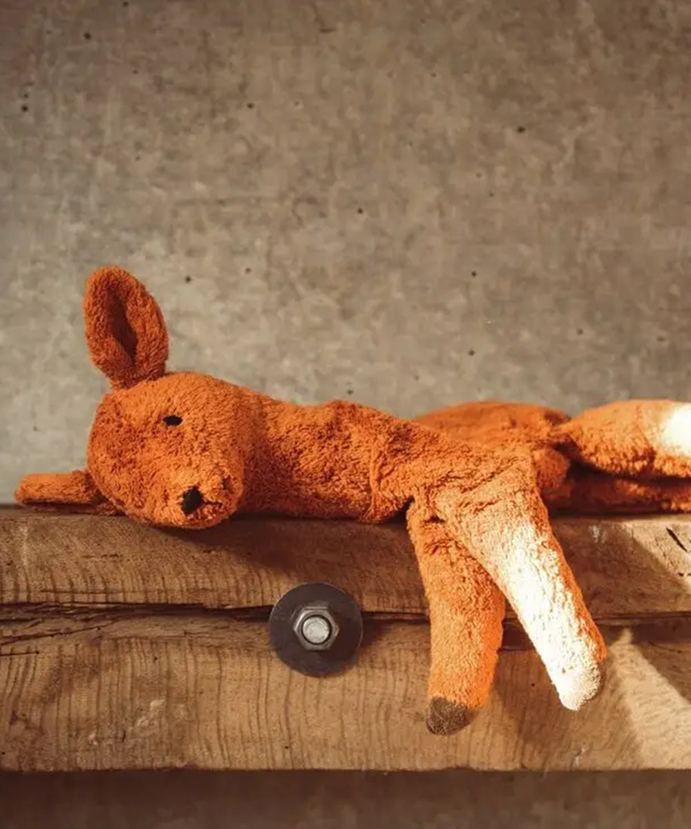 A worn brown Deer stuffed animal lies on a wooden surface against a concrete wall.