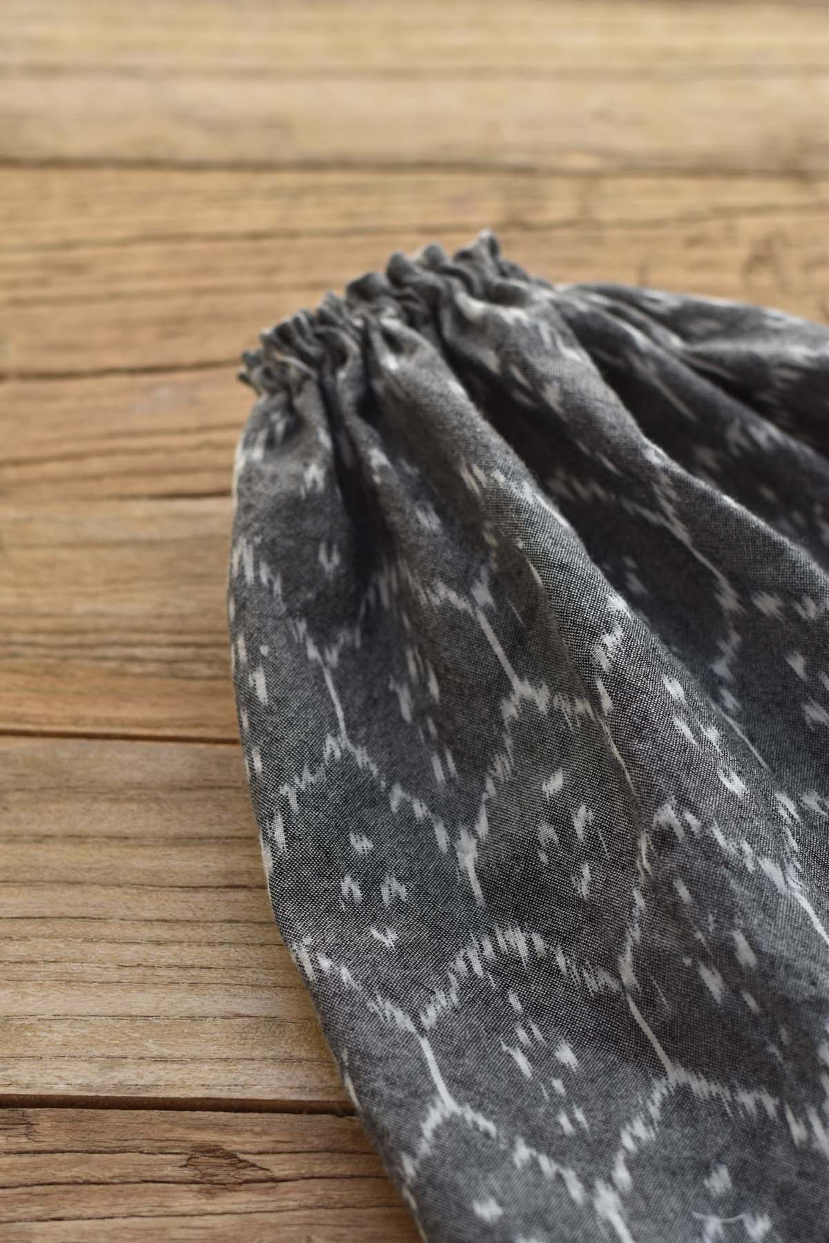 The Fern the Frog – Ikat Field Skirt, featuring gray patterned fabric and an elastic gathered edge, is displayed on a wooden surface.