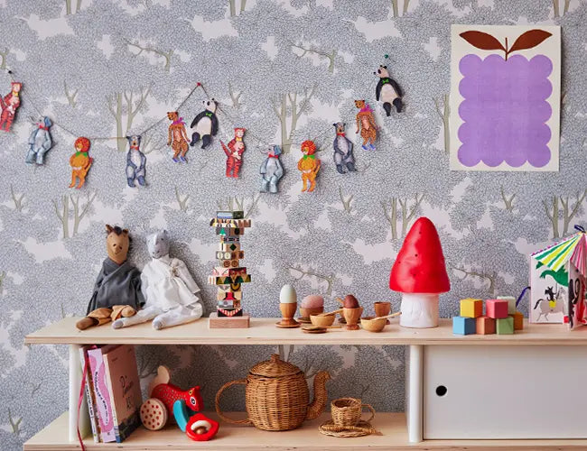 Childrens room with toys, books, a teapot, and decorative items on shelves. Wall has circus-themed garland and a purple abstract art piece.