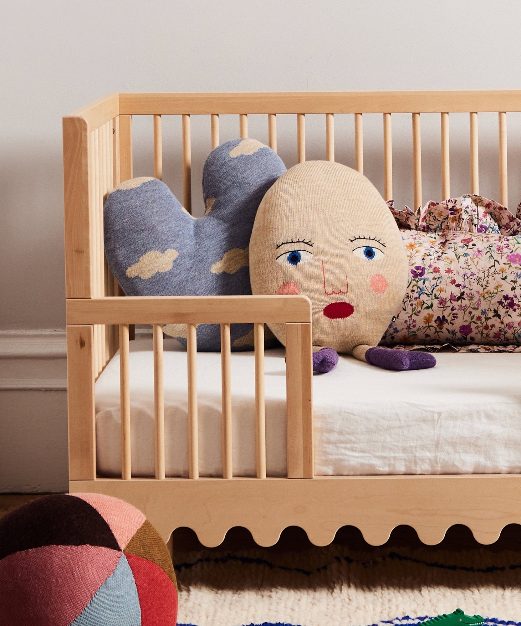 A crib with the Circus Ball - Rose pillow, a face pillow, and a floral pillow on a white mattress.