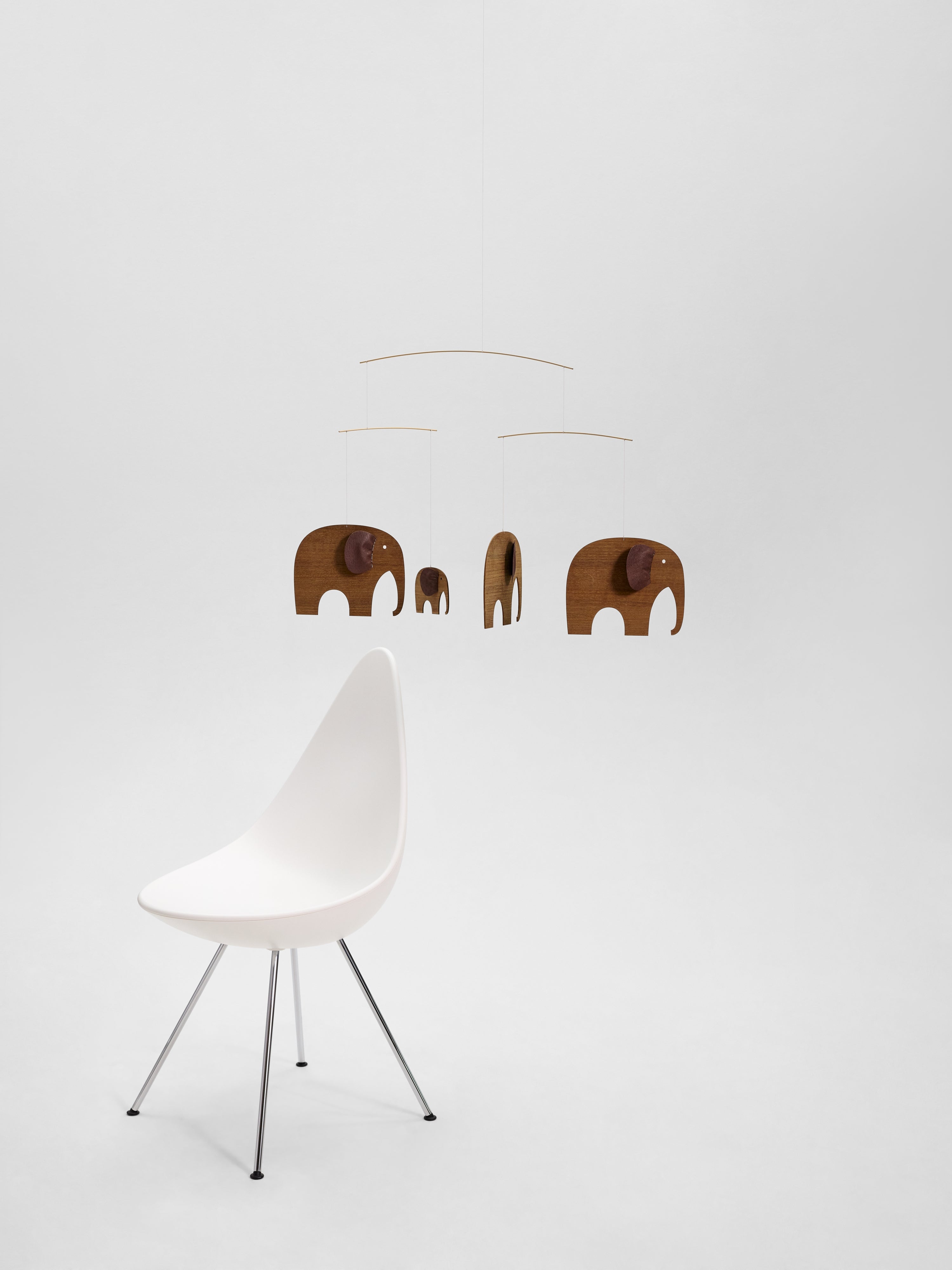 A white chair beside the Elephant Herd 4 | Wood hanging mobile with wooden elephant shapes on a plain white background.
