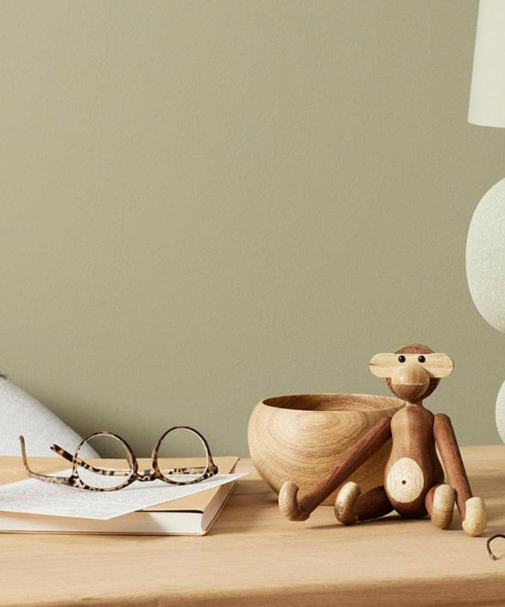 Round glasses on a book, a wooden bowl, and Le Monkey by Kay Bojesen sit on a light wooden table against a beige wall.