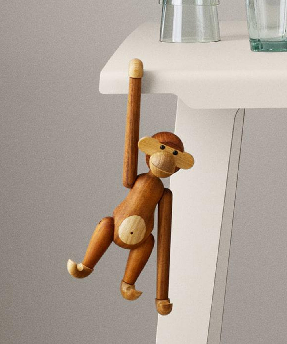 Le Monkey by Kay Bojesen hangs by one arm from the edge of a white table.