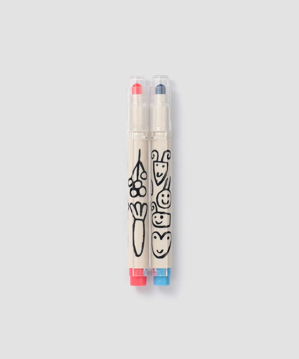 Two Le Well Rounded Markers—one red, one blue—feature playful black doodles and faces on their beige barrels.