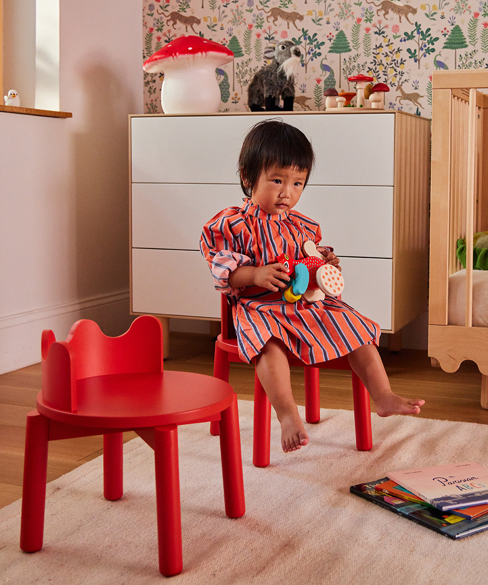 A young child sits on a Moss Chair (Set of 2) in a playful, colorful room, holding toys and looking thoughtfully ahead.