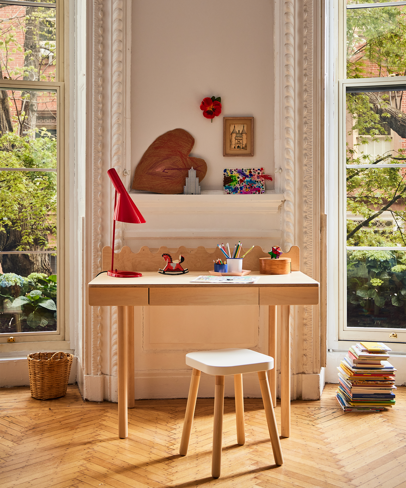 The Moss Desk and a matching stool sit by tall windows, surrounded by art supplies, books, and decor in a bright, cozy room.