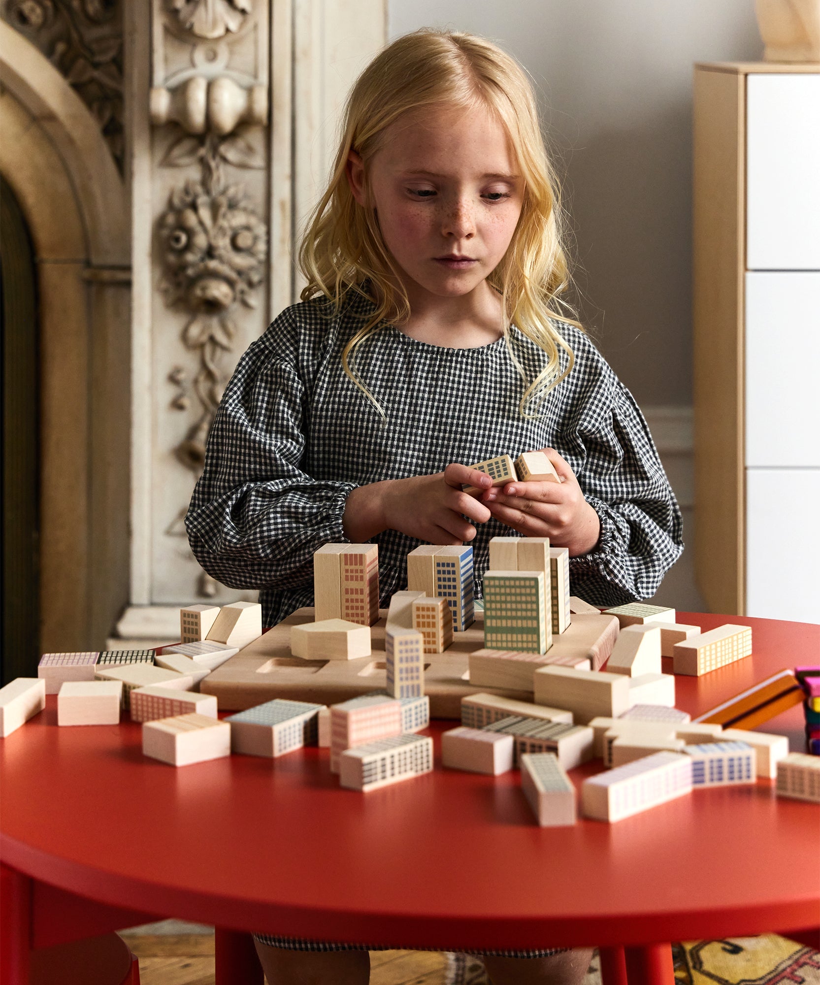 A young girl builds a city with wooden blocks on a Moss Table indoors.