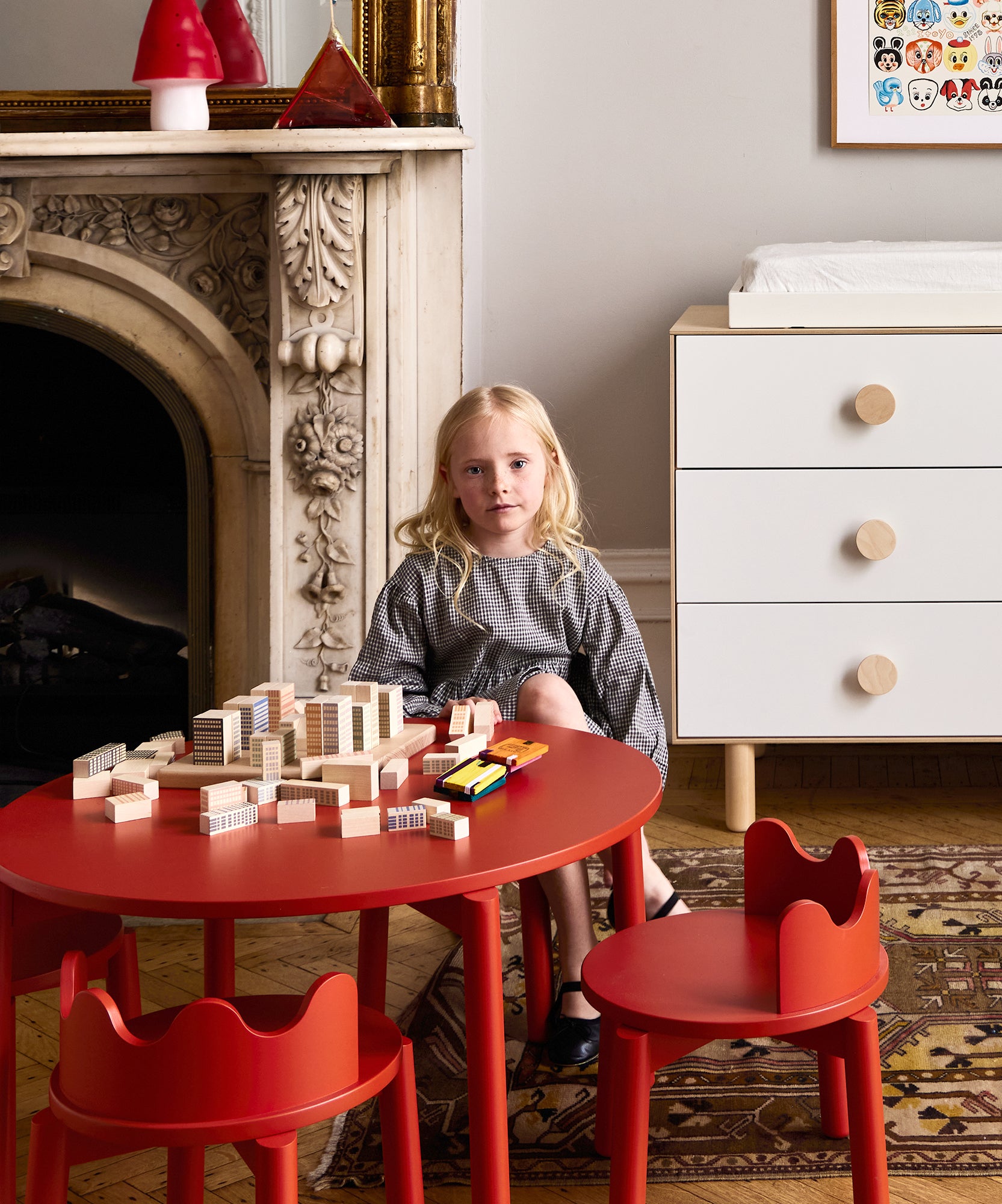 A young girl plays with Le Manhattan Skyline Blocks at a red table in a stylish, modern living room.