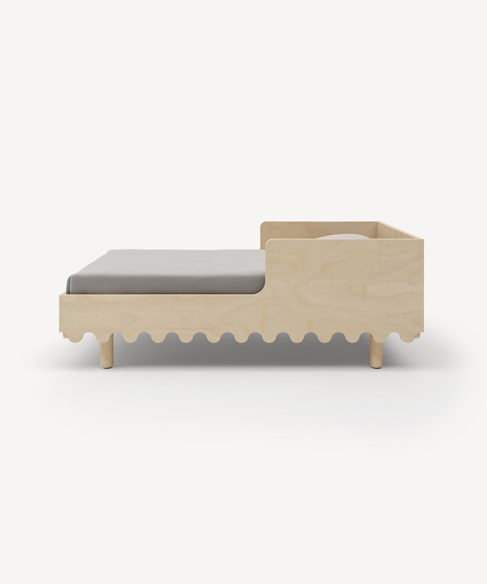 A Moss Toddler Bed featuring a scalloped wooden base and a light gray mattress, angled slightly from the side.
