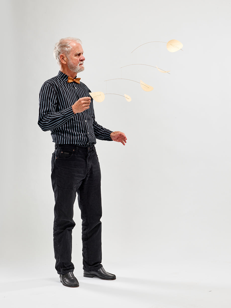 An older man in a striped shirt admires the Drifting Clouds Nature mobile (Size M) against a plain background.