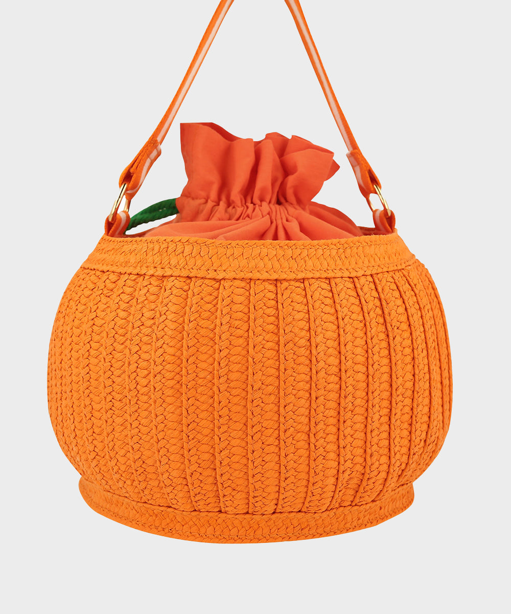 The Le Pumpkin Basket Bag is a round, orange woven handbag with a drawstring closure, inspired by the shape of a pumpkin.