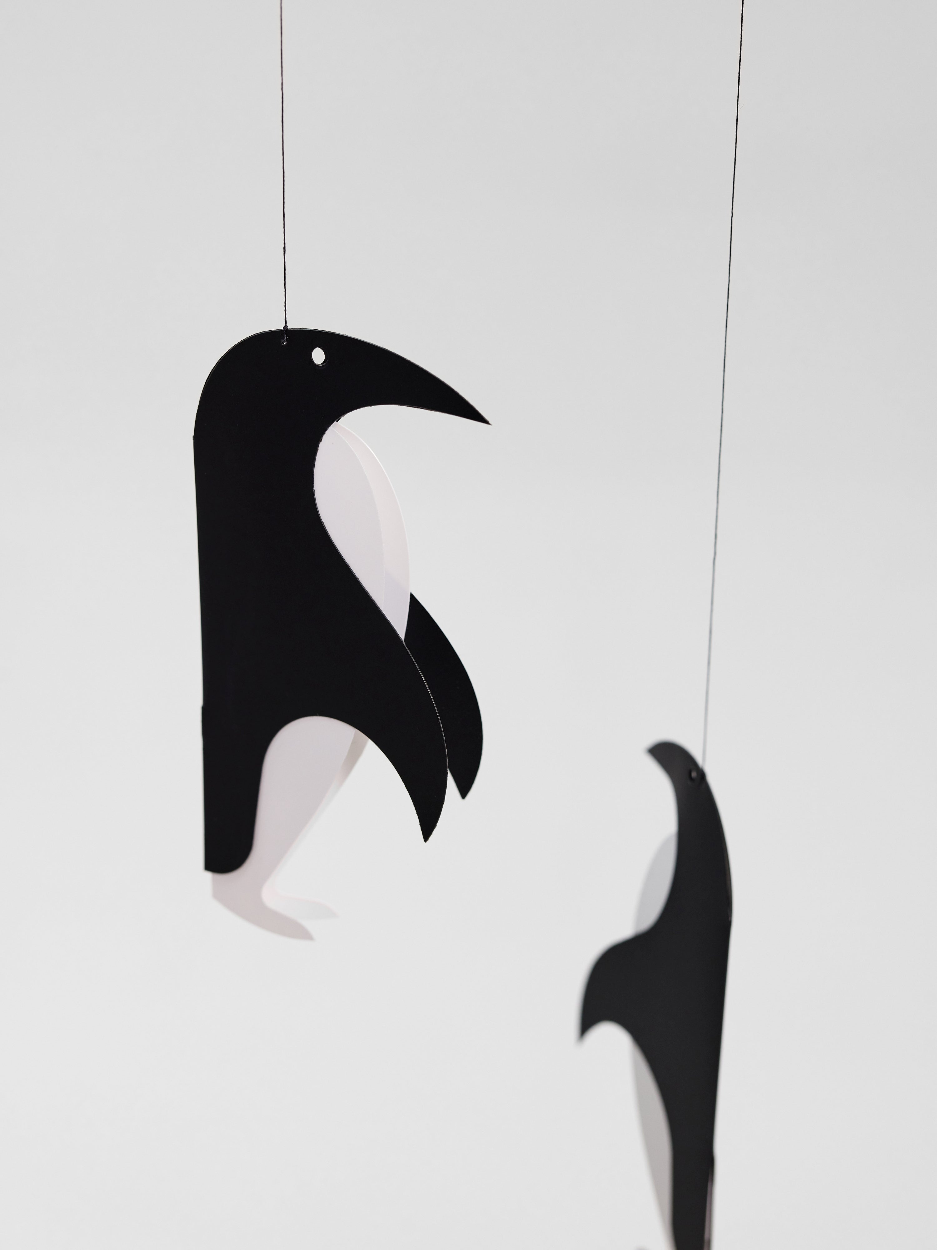 Two Penguin Talk black and white paper penguin mobiles are hanging against a plain white background.
