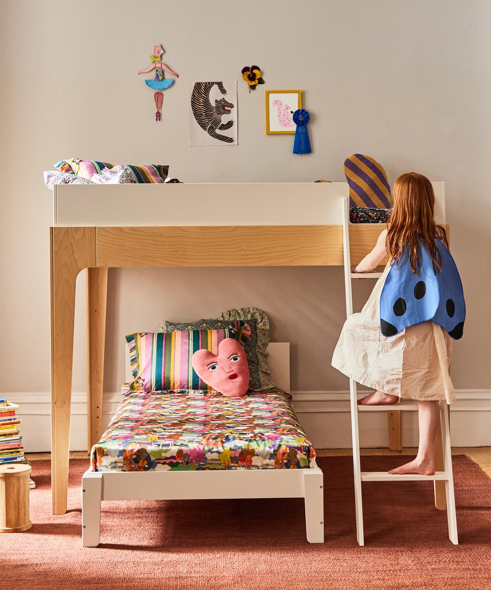 A child in a ladybug cape climbs a loft above a colorful Perch Twin Bed in a cozy bedroom.