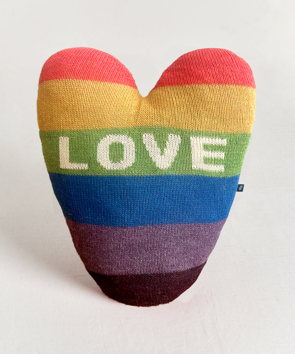 The Heart Pillow - Rainbow features rainbow stripes and "LOVE" in white letters across the center.