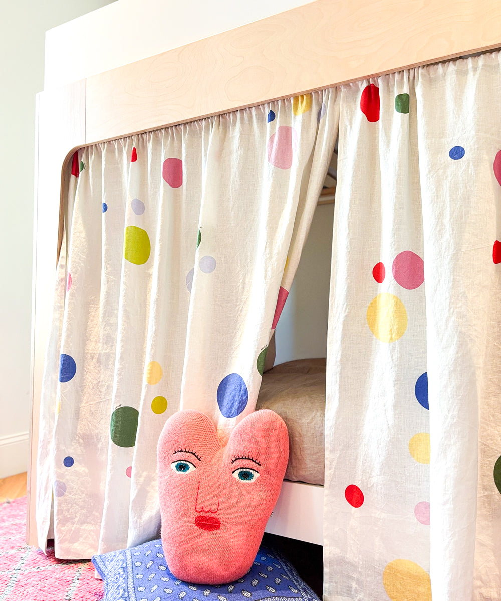Printed Perch Bunk/Loft Linen Curtains with colorful polka dots hanging from a bunk bed, with a pink heart-shaped face pillow in front.
