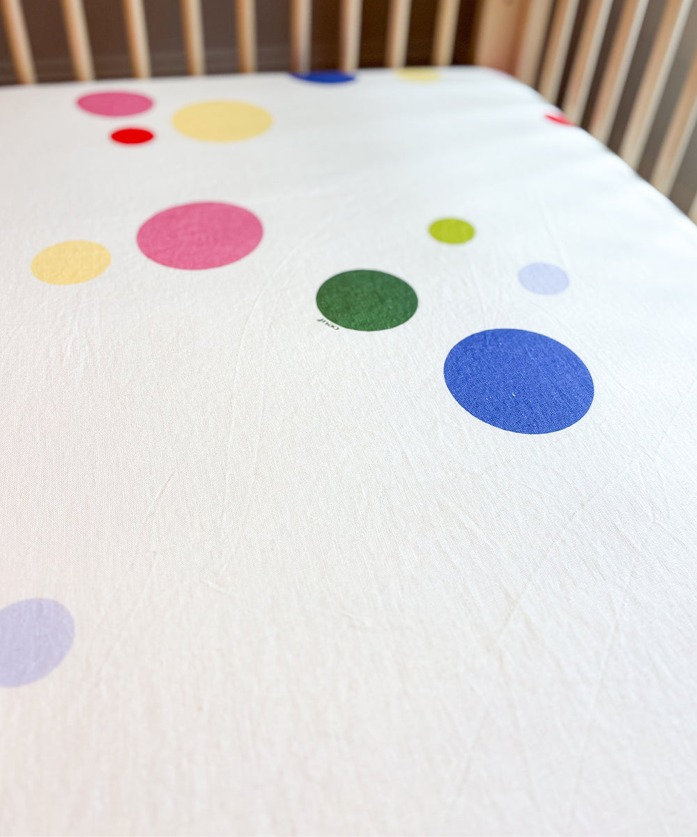Printed Linen Crib Sheet featuring a white background with a pattern of colorful polka dots.