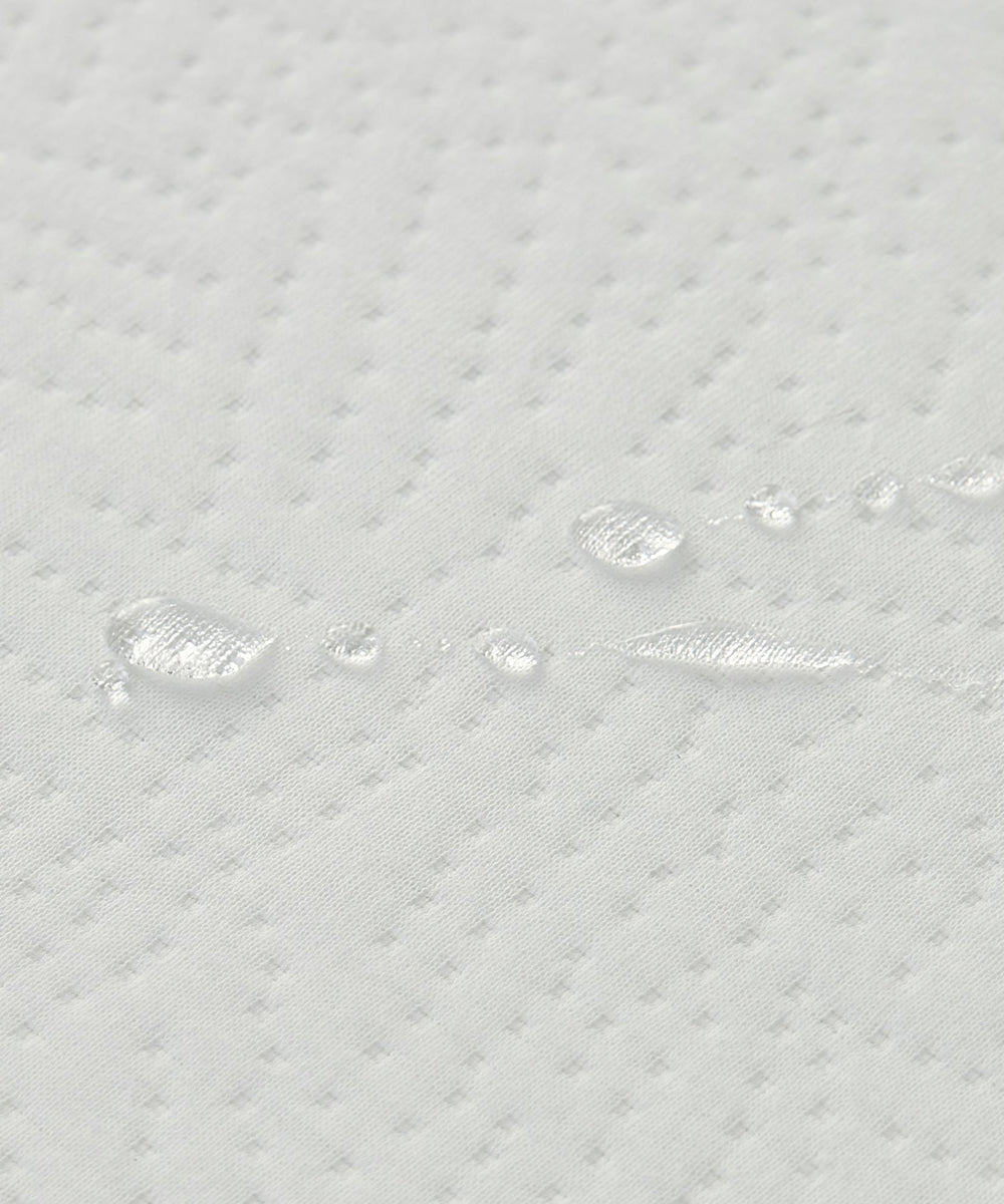 Close-up of water droplets on the Dual Firm Crib Mattress's white, quilted, dotted fabric surface.