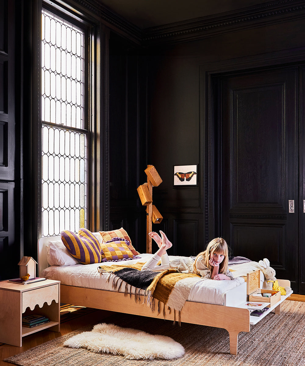 Child resting on a Dual Firm Twin Full-Size Mattress in a chic, dark-walled room with a large window and wooden decor accents.