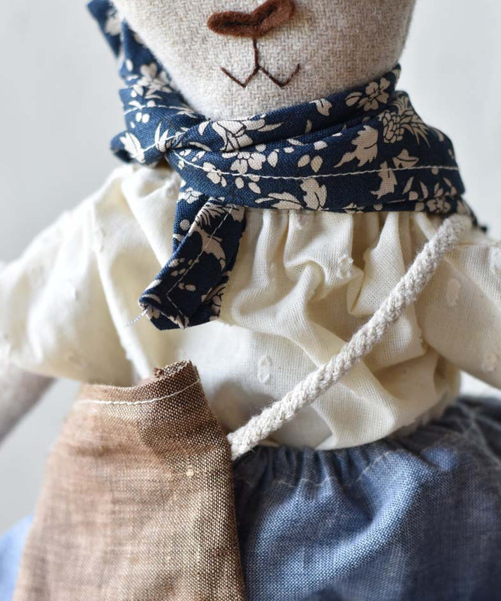Ruthie le Rabbit is a fabric doll with a blue floral scarf, cream blouse, blue skirt, and a brown bag over her shoulder.