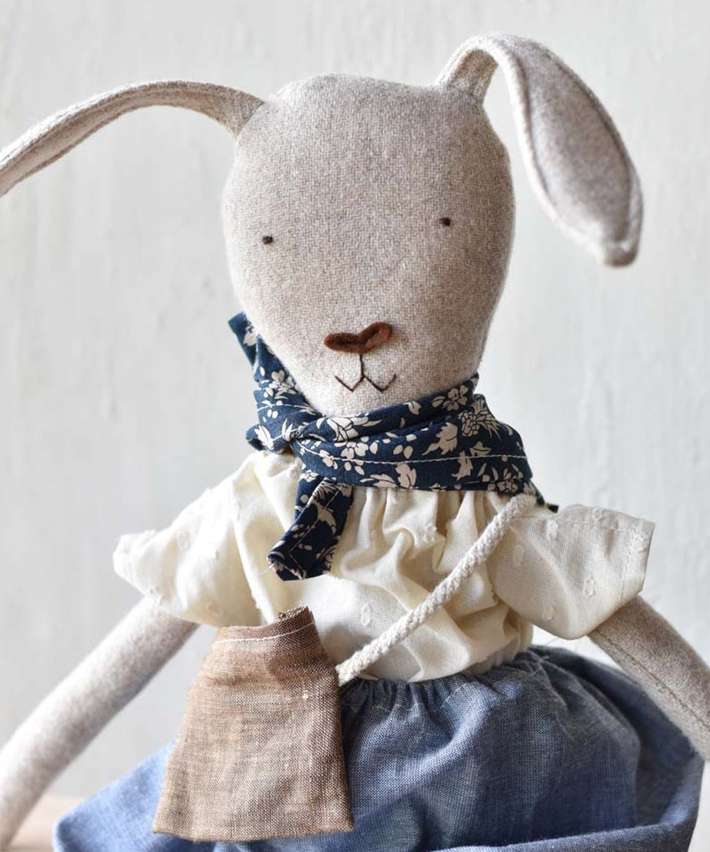 Ruthie le Rabbit is a stuffed bunny toy dressed in a blue skirt, cream blouse, floral scarf, and a small brown bag.