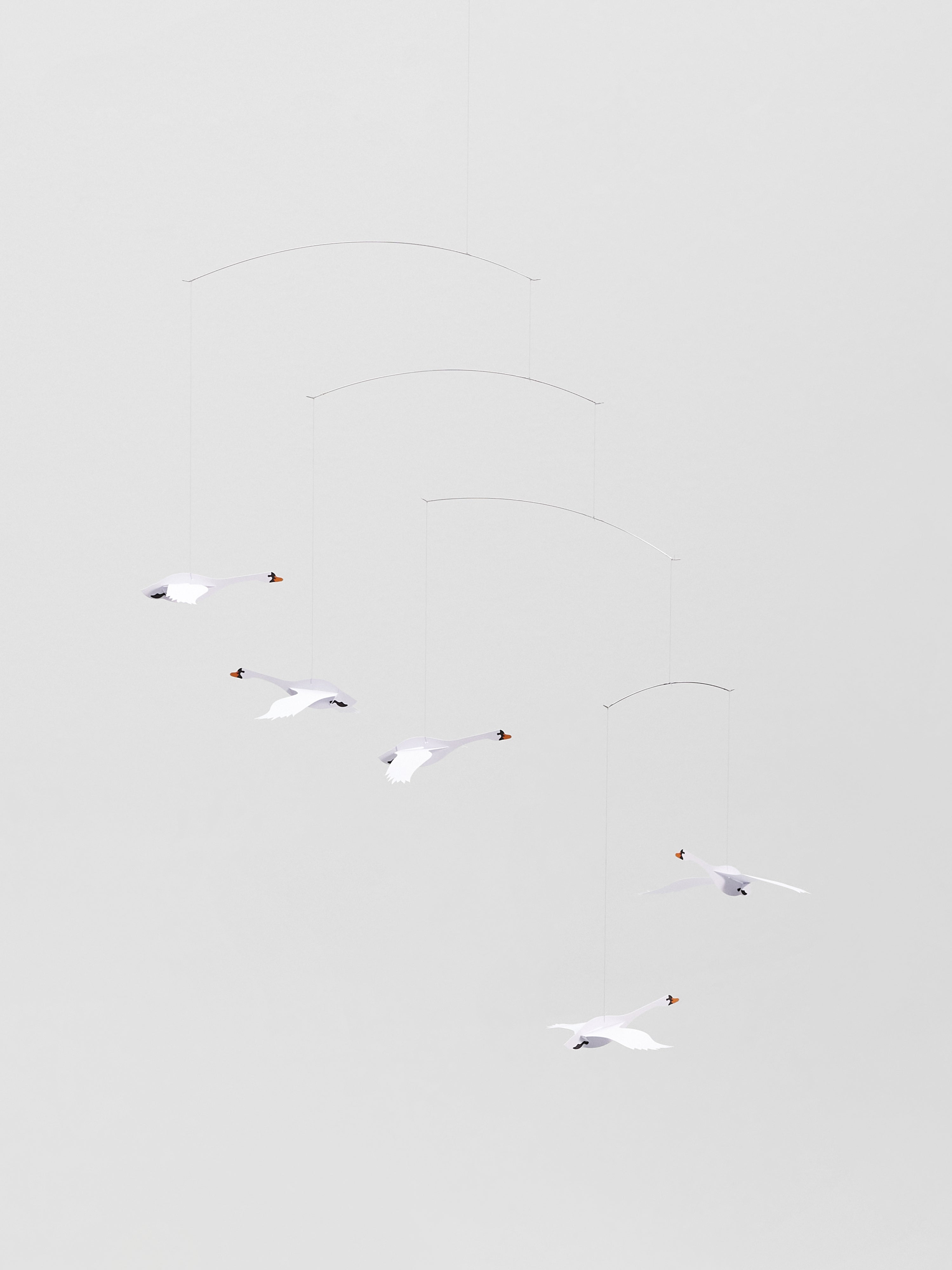 Five Scandinavian Swans mobiles hang in midair against a plain, light gray background.