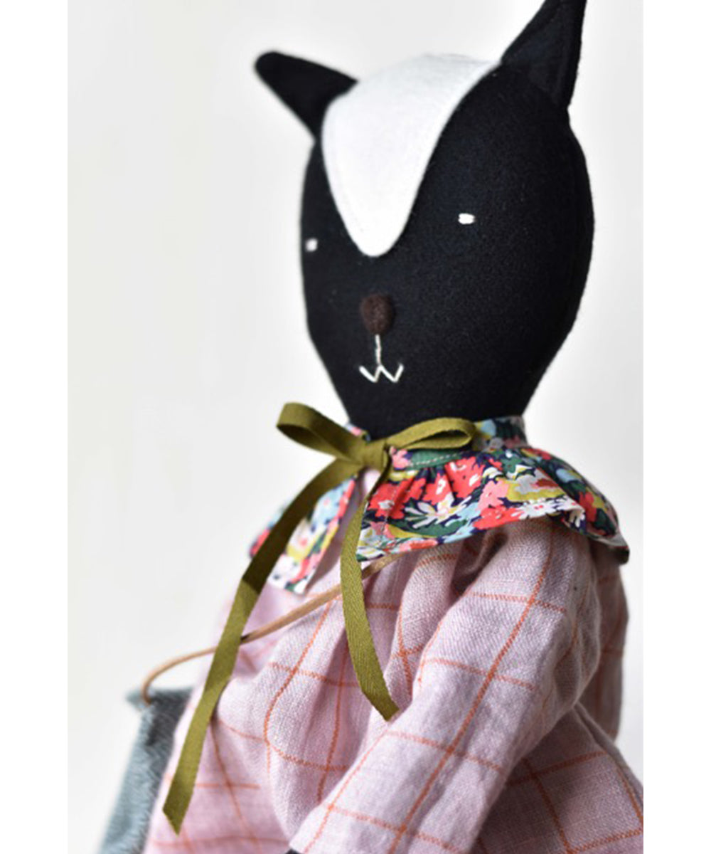 Scout le Skunk is a stuffed animal skunk doll dressed in a pink checkered dress, floral collar, and green ribbon bow.